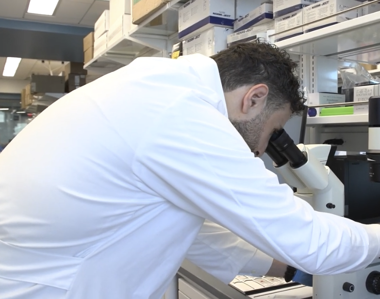 scientist in lab coat looking through microscope