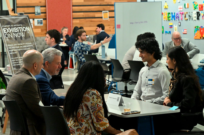 At the Hatchery, a student stands and talks with two students sitting on swings