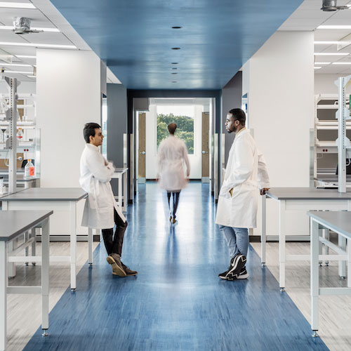 Two men in lab coats facing one another in a large, bright laboratory