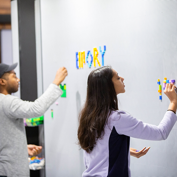 two students placing colorful tiles onto a large board to spell words