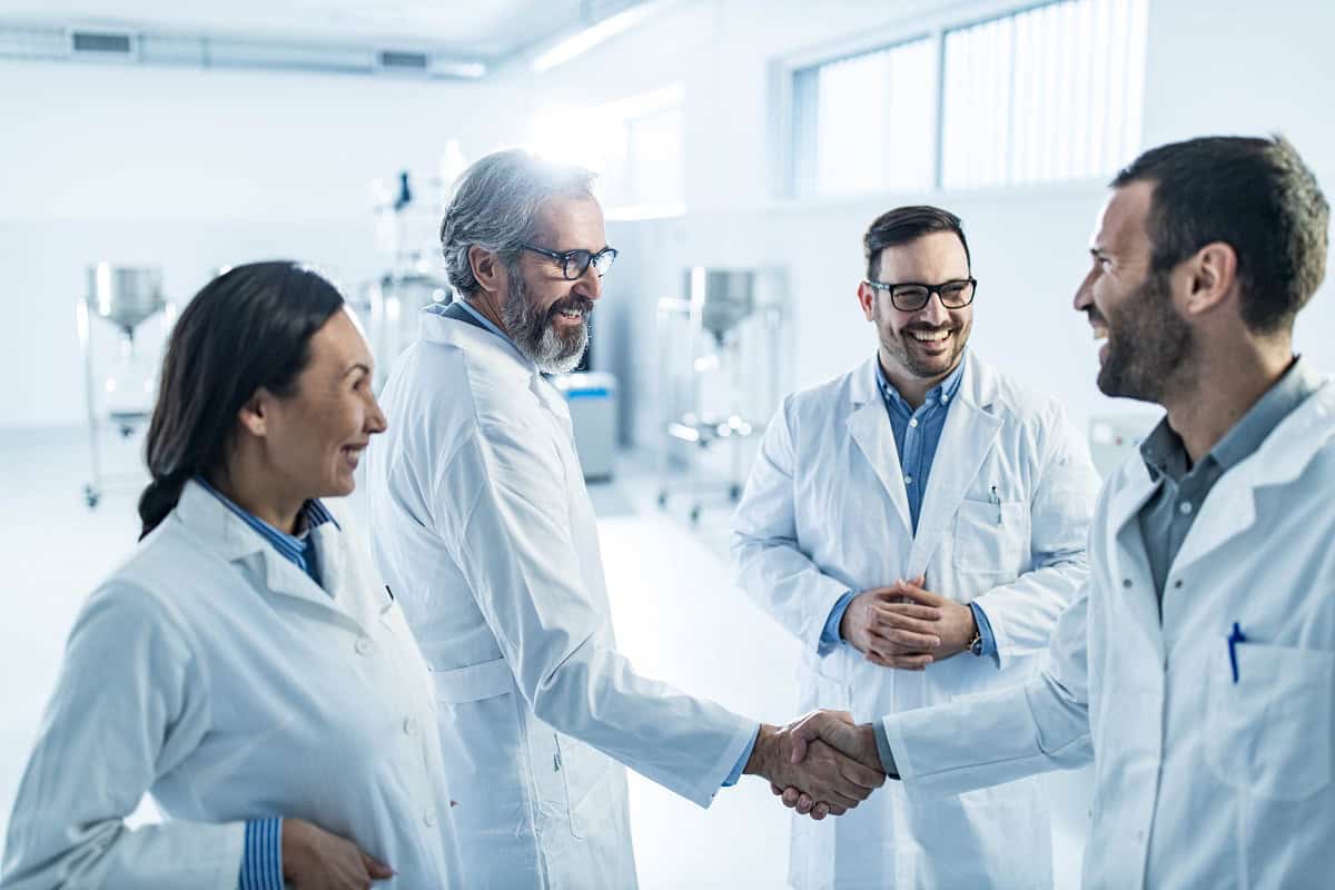 four people smiling in white lab coats, two shaking hands