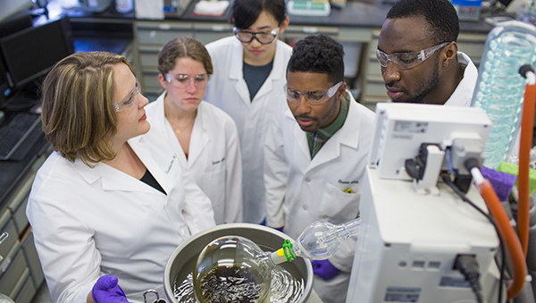 Researchers in white lab coats peering into a glass vessel